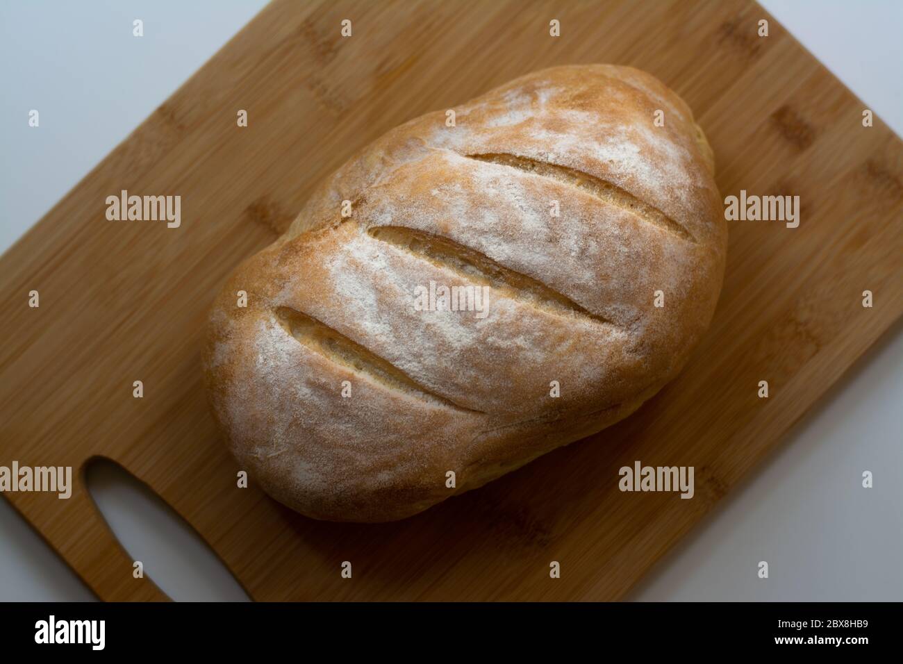 Un pain de pain de levain cuit maison avec trois coupes parallèles sur une planche à découper en bois avec une serviette de cuisine Banque D'Images