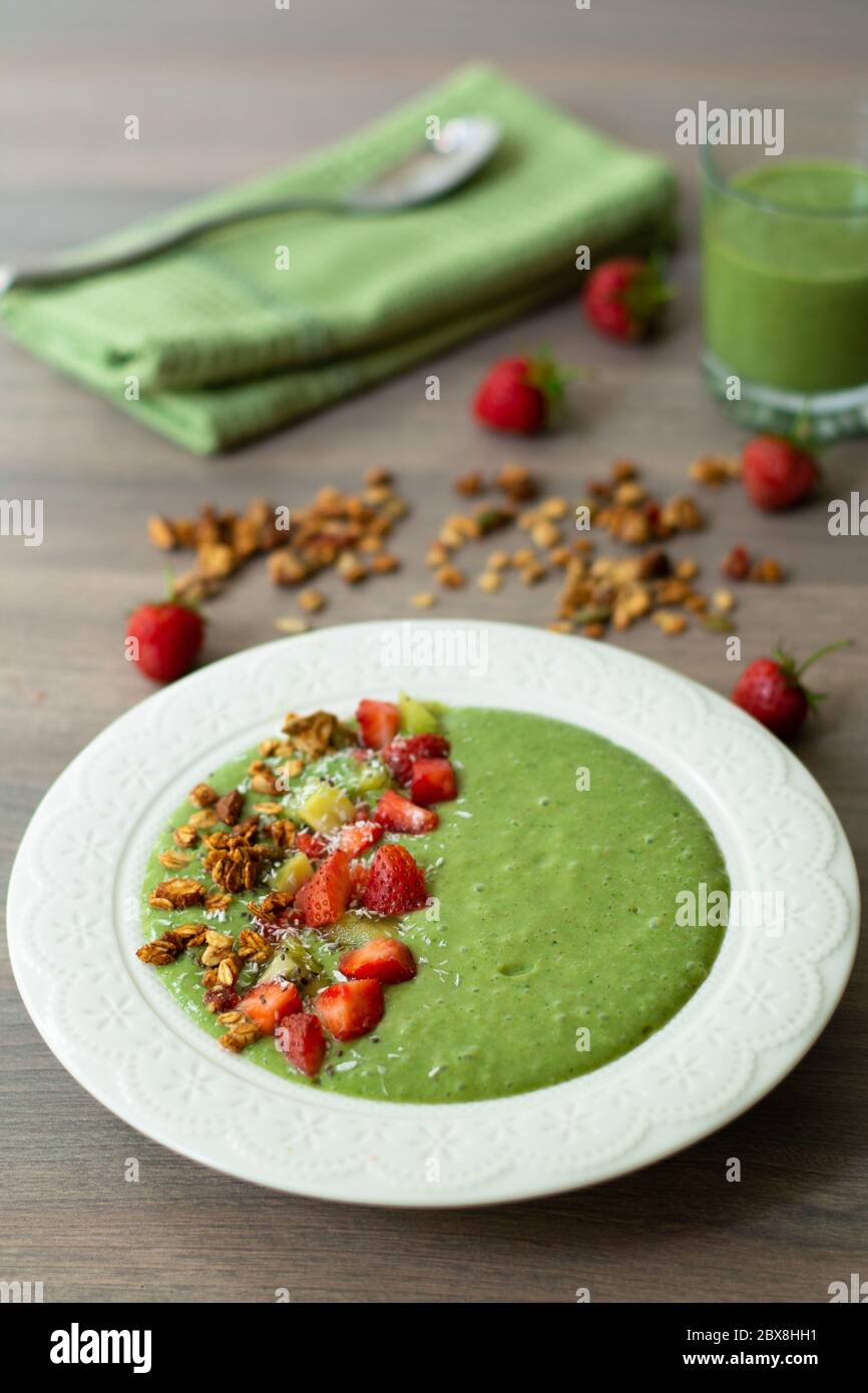 Bol à smoothie vert avec banane, fraise, épinards, chou vert, kiwi, lait de coco garni d'avoine maison, granola aux noix et graines, flocons de noix de coco, chia Banque D'Images