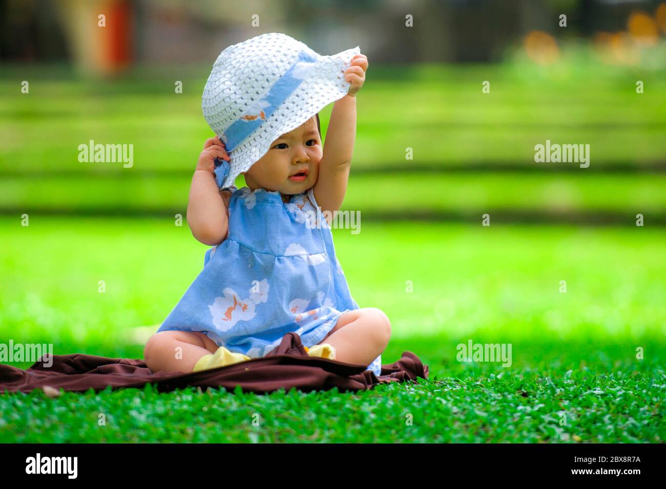 Portrait Candide Isole D Une Petite Fille Coreenne Asiatique Douce Et Adorable De 3 Ou 4 Mois Jouant Avec Un Chapeau Seul Dans Le Parc De La Ville Assise Sur L Herbe Verte Photo