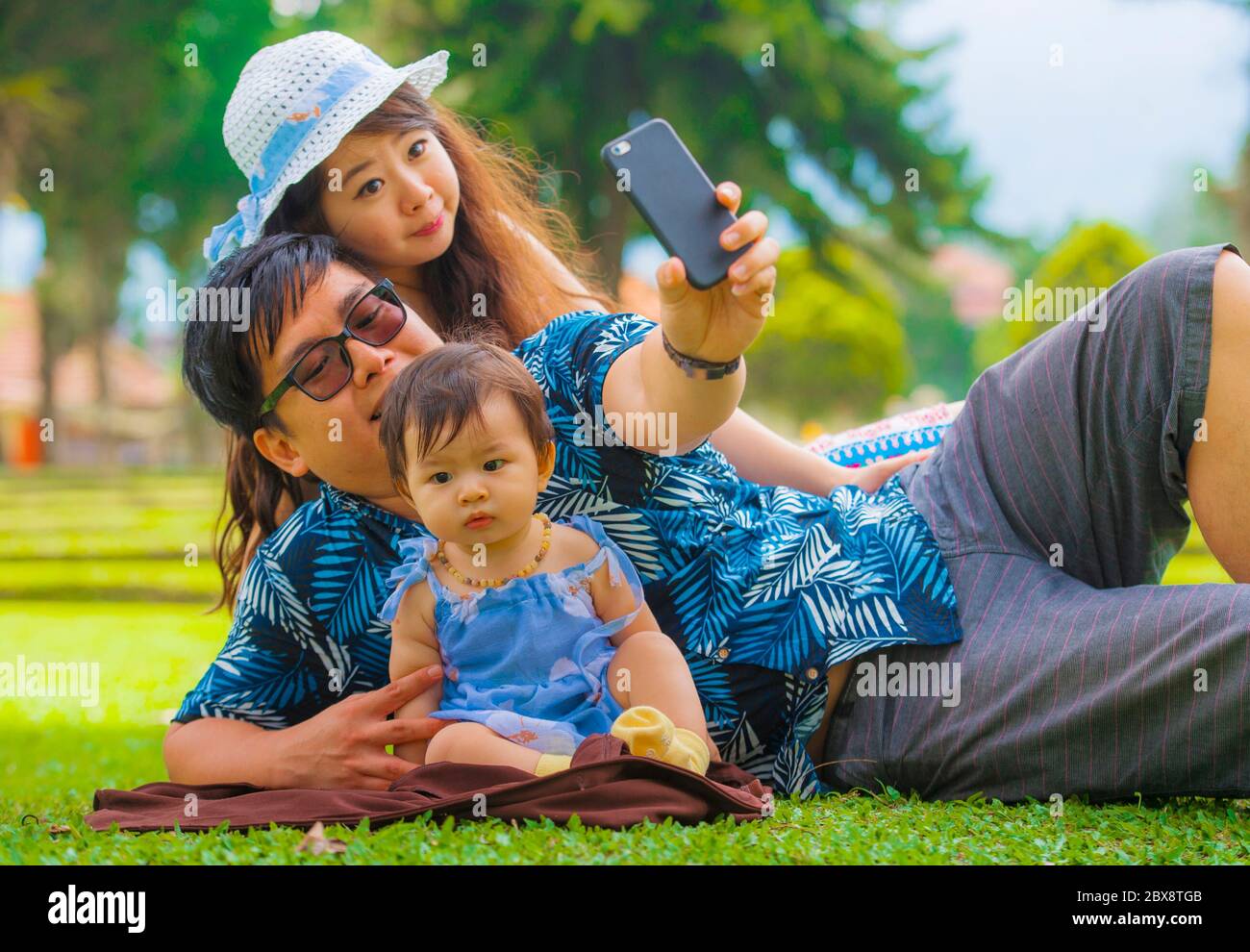Jeune famille japonaise asiatique heureuse et aimante avec parents et petite fille douce au parc de la ville avec le père prenant le selfie pic avec téléphone portable Banque D'Images