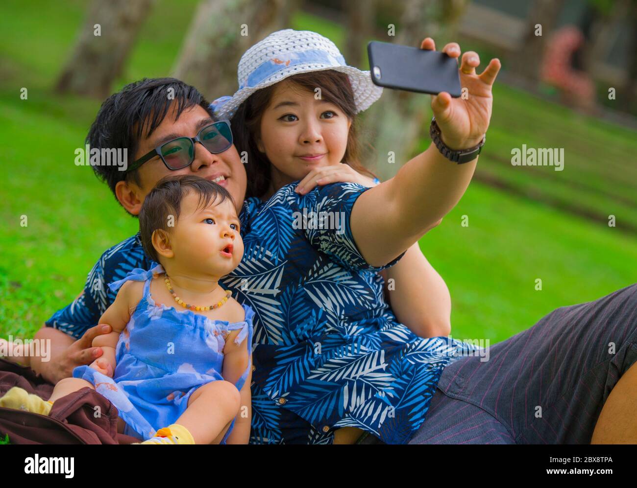 Jeune famille coréenne asiatique heureuse et aimante avec parents et petite fille douce au parc de la ville avec le père prenant le selfie pic avec téléphone mobile Banque D'Images