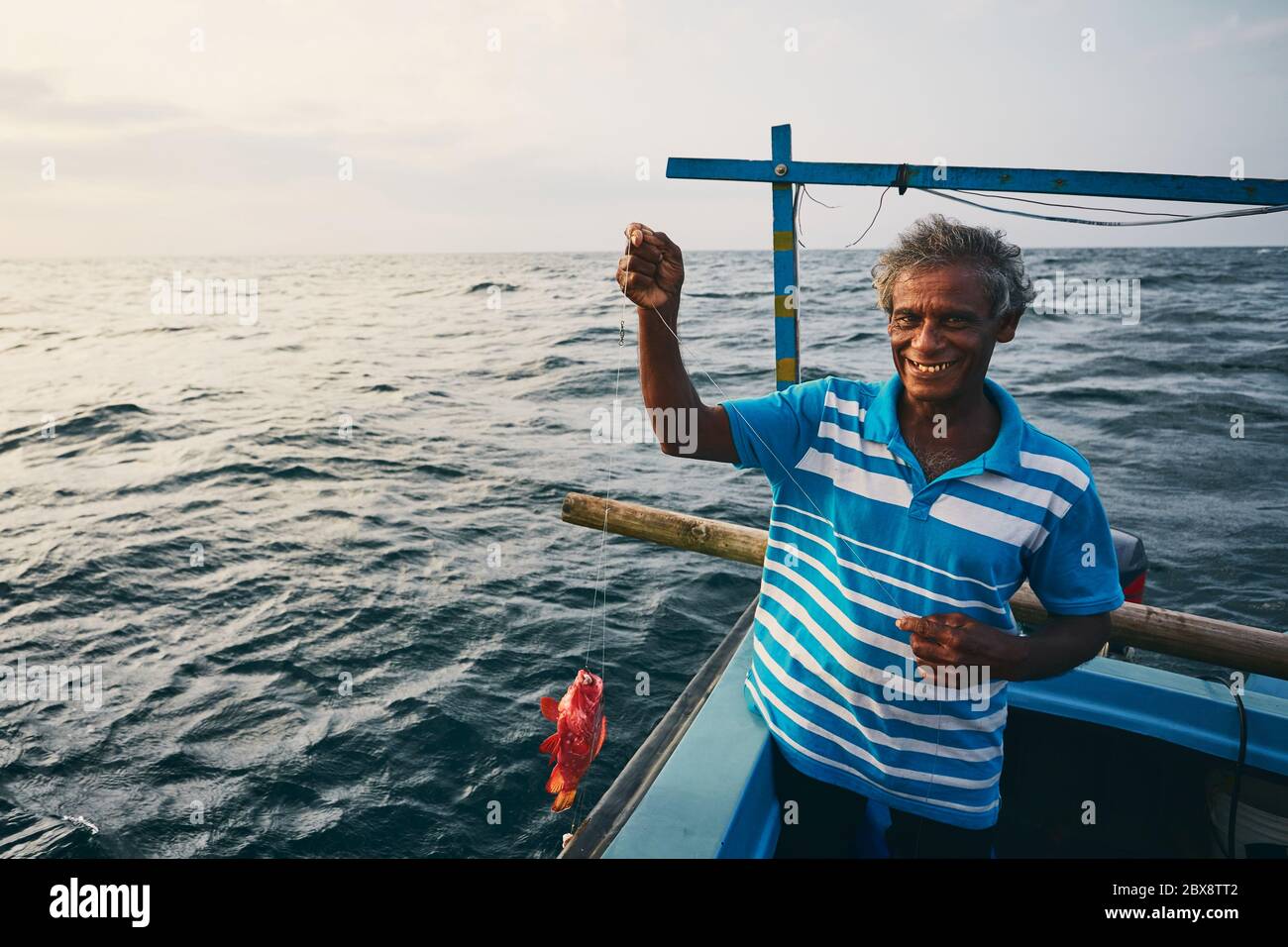 Pêcheur senior tenant du poisson rouge sur un bateau de pêche près de la côte du Sri Lanka. Banque D'Images