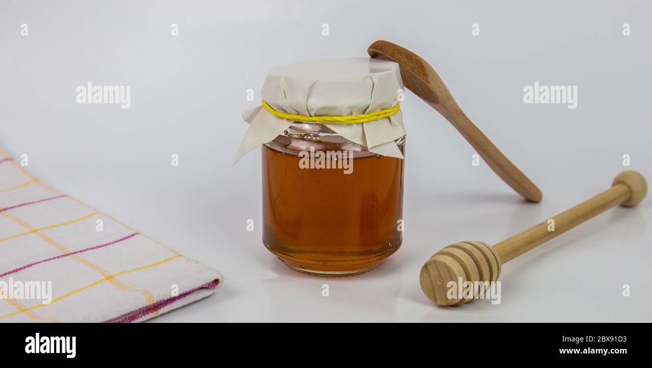 Pot en verre avec miel et bâton de bois sur fond blanc Banque D'Images