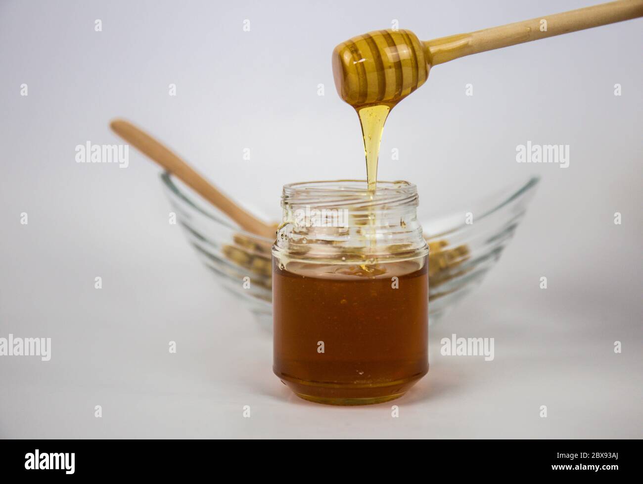 Pot en verre avec miel et bâton de bois sur fond blanc. Verser le miel aromatique dans le bol, fermer. Banque D'Images