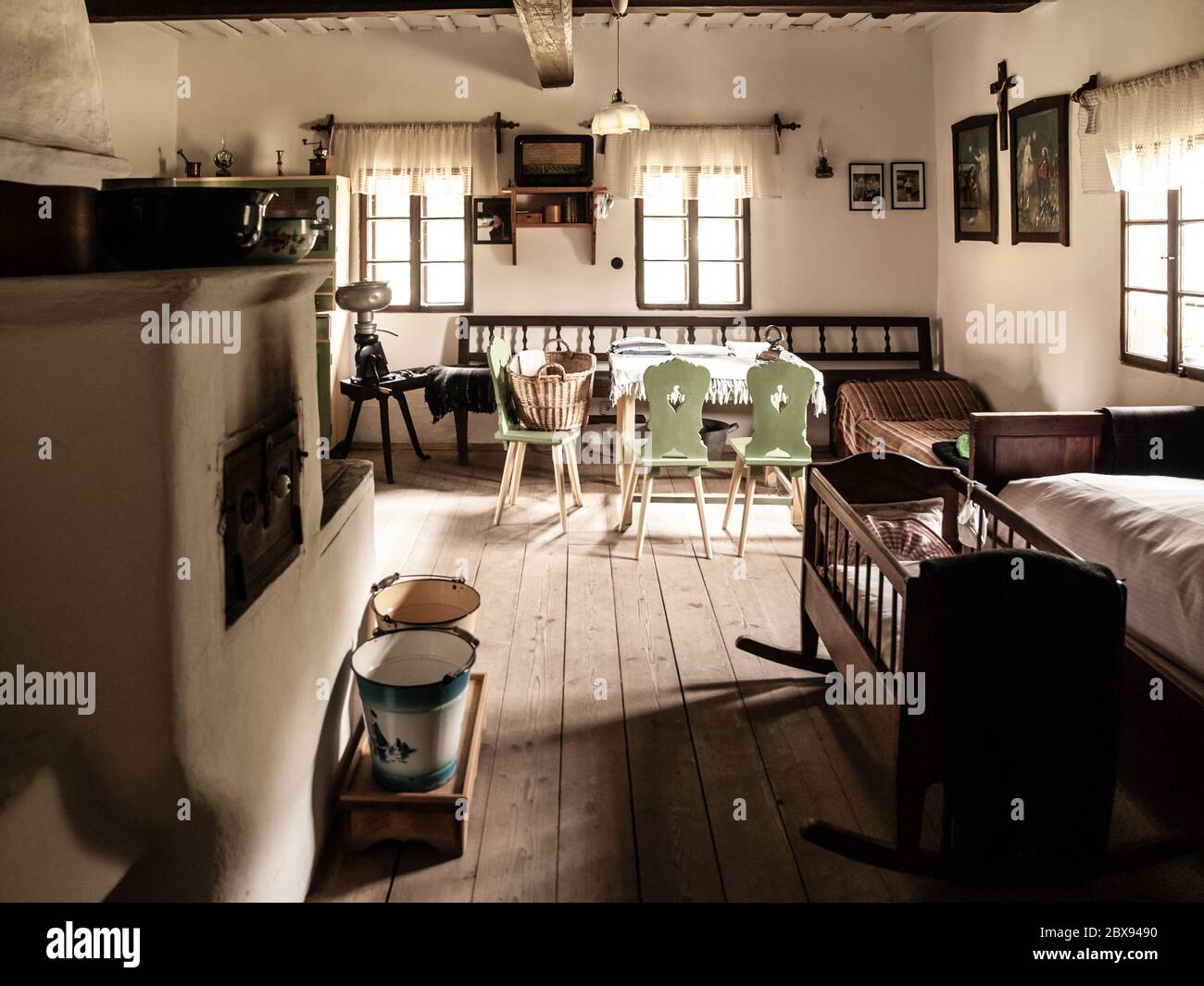 Chambre vintage avec lit, berceau, four, table et chaises dans la maison rurale ancienne. Image de style sépia. Banque D'Images