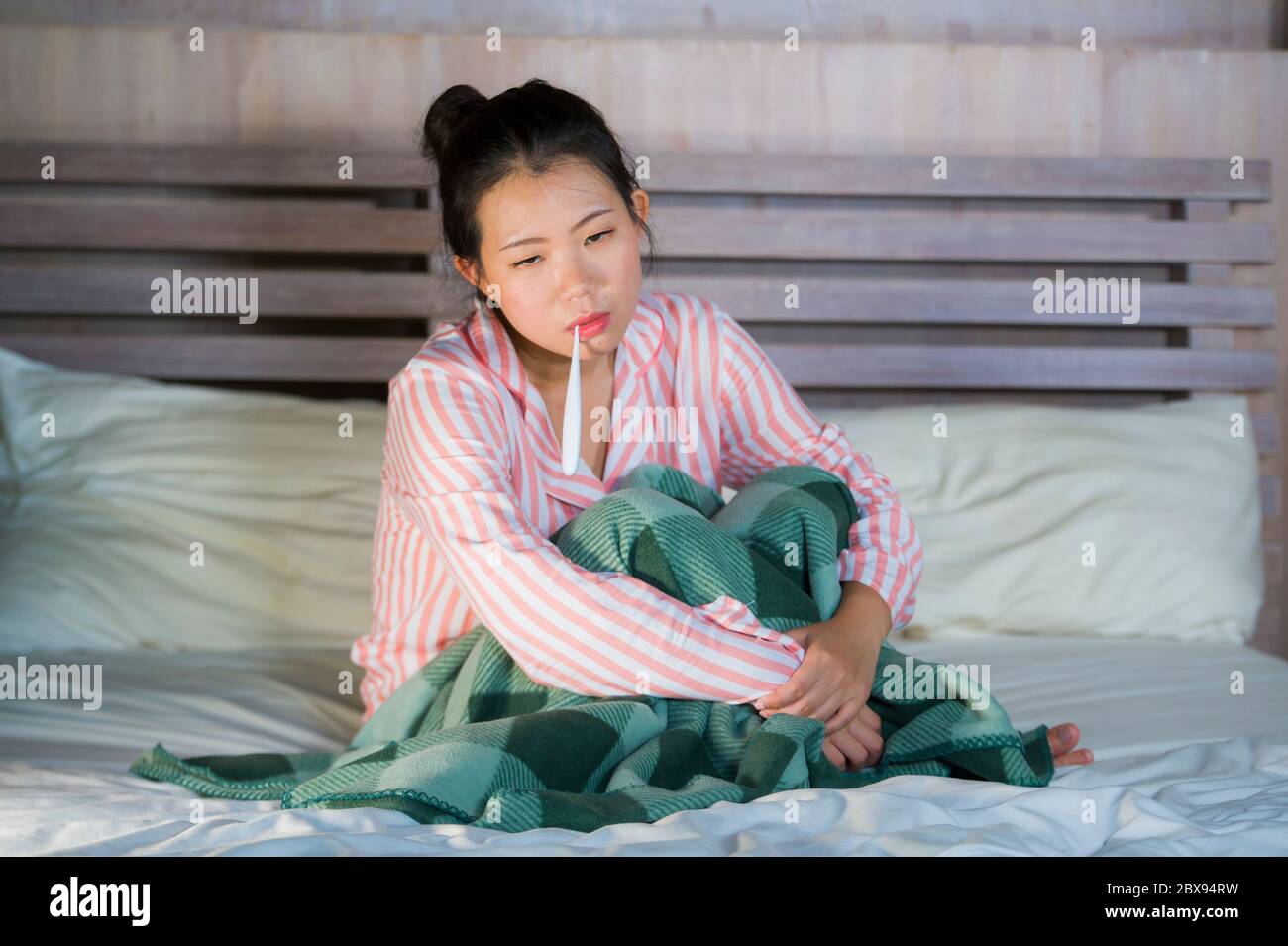 Jeune belle et douce asiatique femme chinoise en pyjama se sentant malade à  la maison chambre à coucher souffrant de froid et de grippe prenant la  température avec thermomètre dans l'être Photo