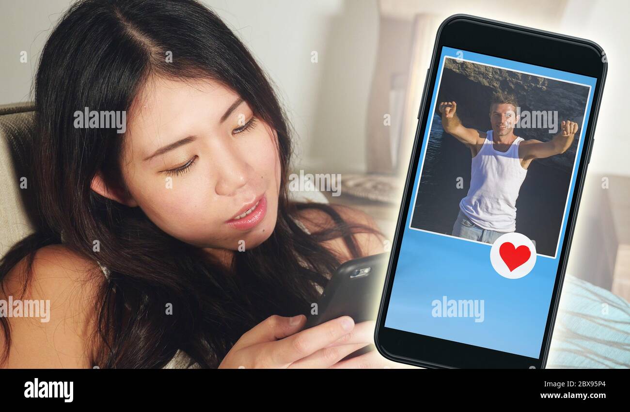 Jeune femme asiatique belle et heureuse coréenne en utilisant l'application de rencontres en ligne sur le téléphone mobile en envoyant comme message à beau Caucasien homme recherche Banque D'Images