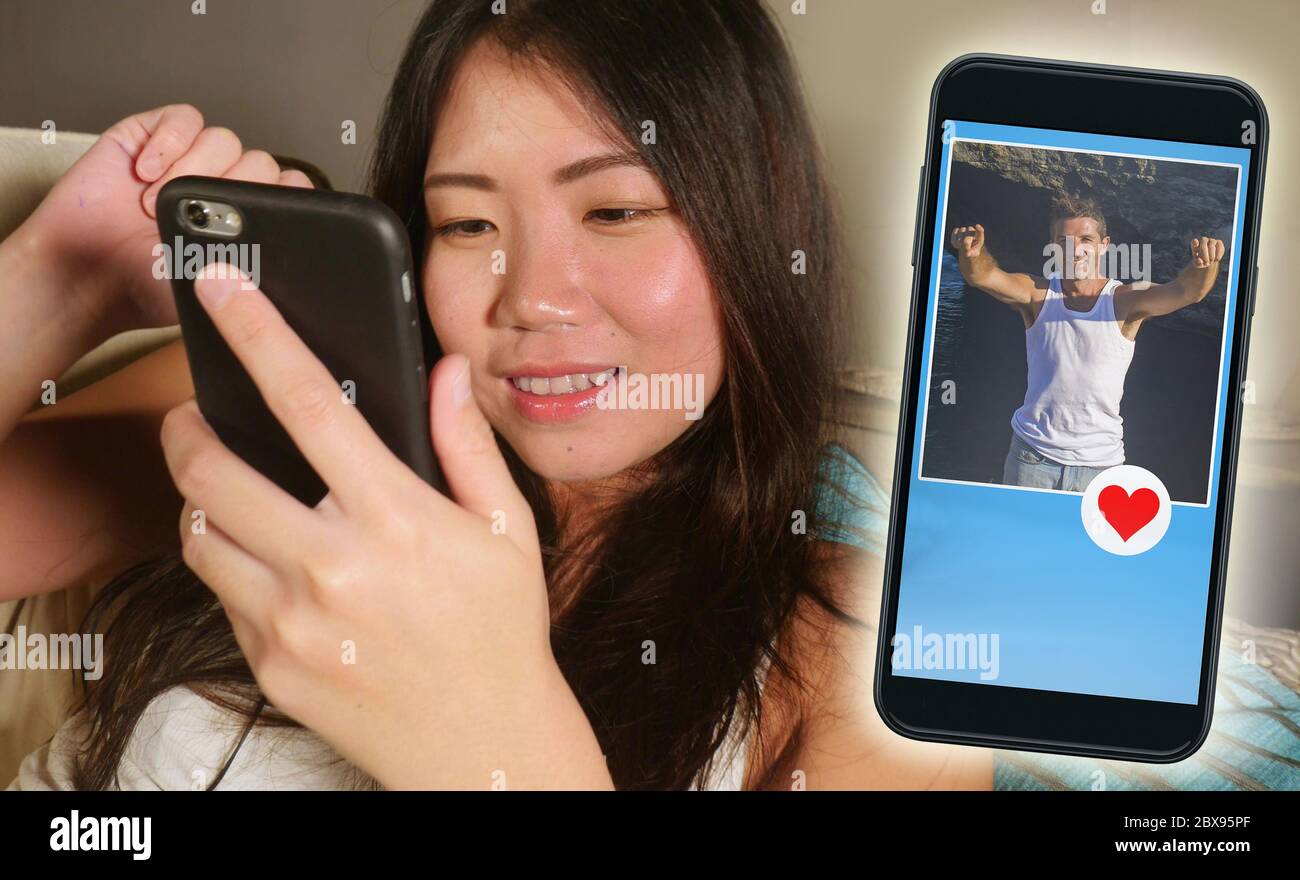 Jeune fille asiatique belle et heureuse en utilisant l'application de rencontres en ligne sur le téléphone mobile en envoyant un message à beau Caucasien homme recherche Banque D'Images