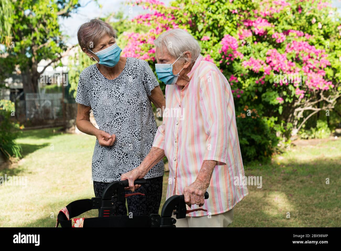 Soignant aidant la femme âgée à obtenir l'exercice dans le jardin portant le masque Banque D'Images