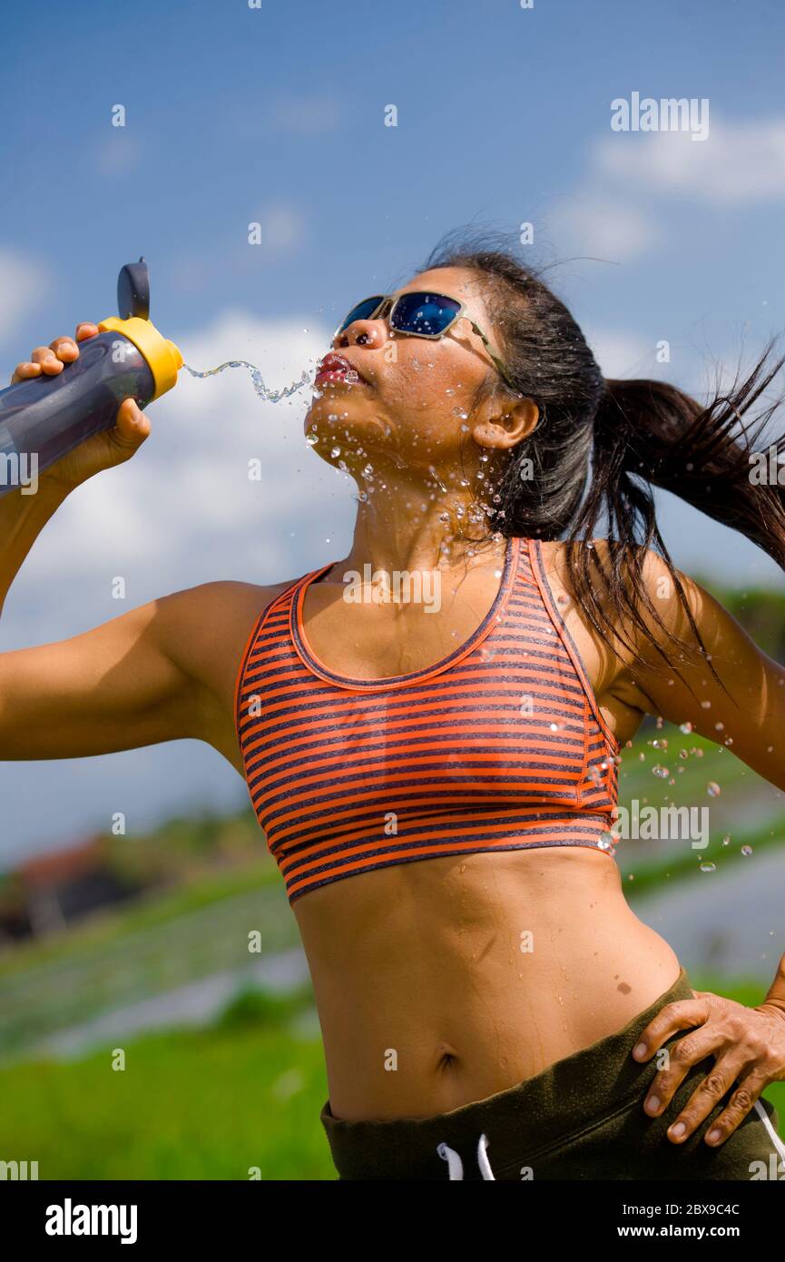 Attrayante et adaptée asiatique coureur femme tenant une bouteille isotonique eau potable après l'entraînement et la série de course entraînement à l'extérieur sur piste en fiel vert Banque D'Images