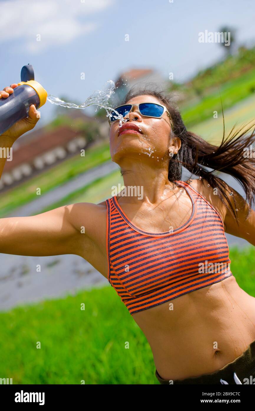 Attrayante et adaptée asiatique coureur femme tenant une bouteille isotonique eau potable après l'entraînement et la série de course entraînement à l'extérieur sur piste en fiel vert Banque D'Images