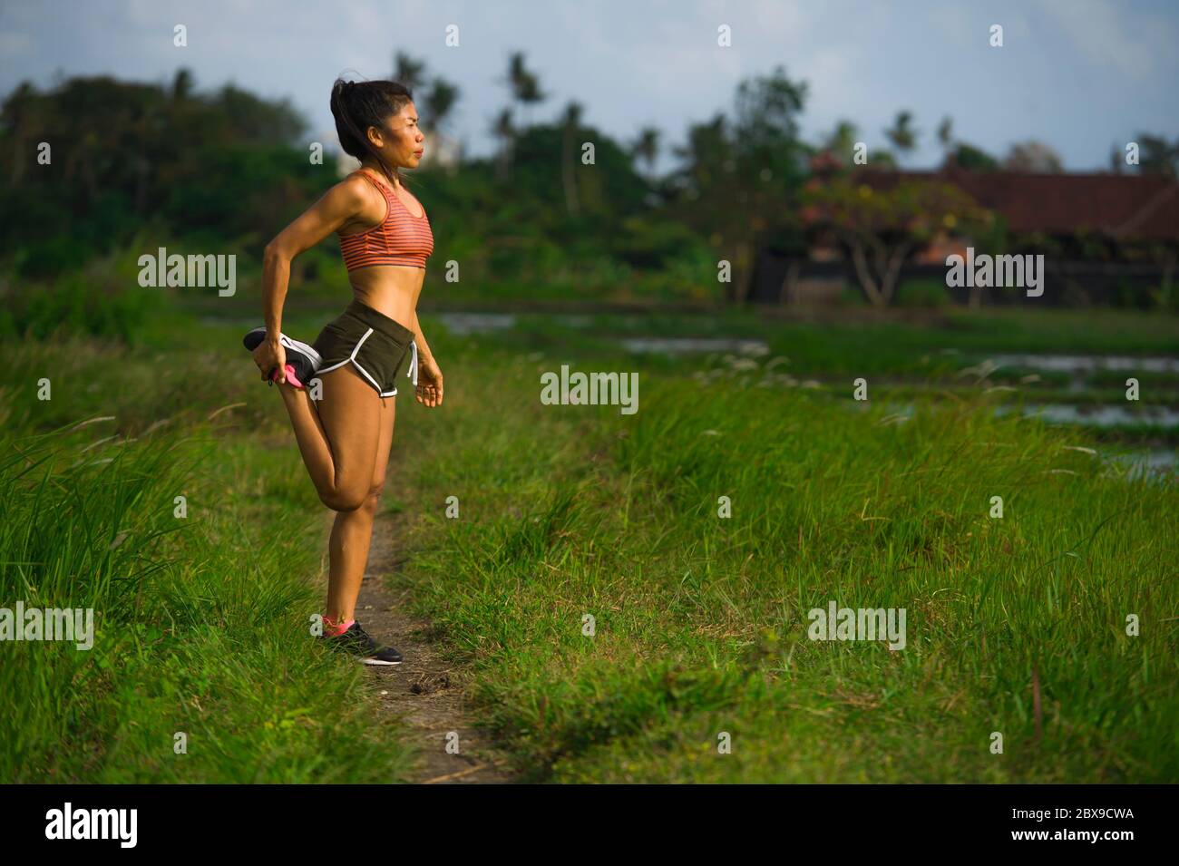 Forme et sportif coureur d'âge moyen femme asiatique qui s'étend sur les jambes et le corps après l'entraînement sur terrain vert magnifique en entraînement sportif et Banque D'Images