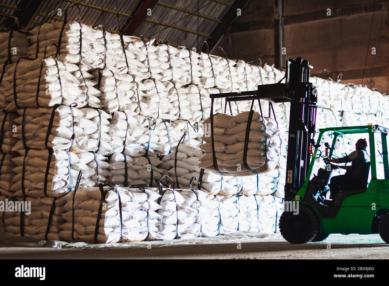 Chariot élévateur porte un sac jumbo de sucre blanc raffiné à mettre sur la pile à l'intérieur de l'entrepôt. Exploitation et gestion des entrepôts de sucre. Banque D'Images