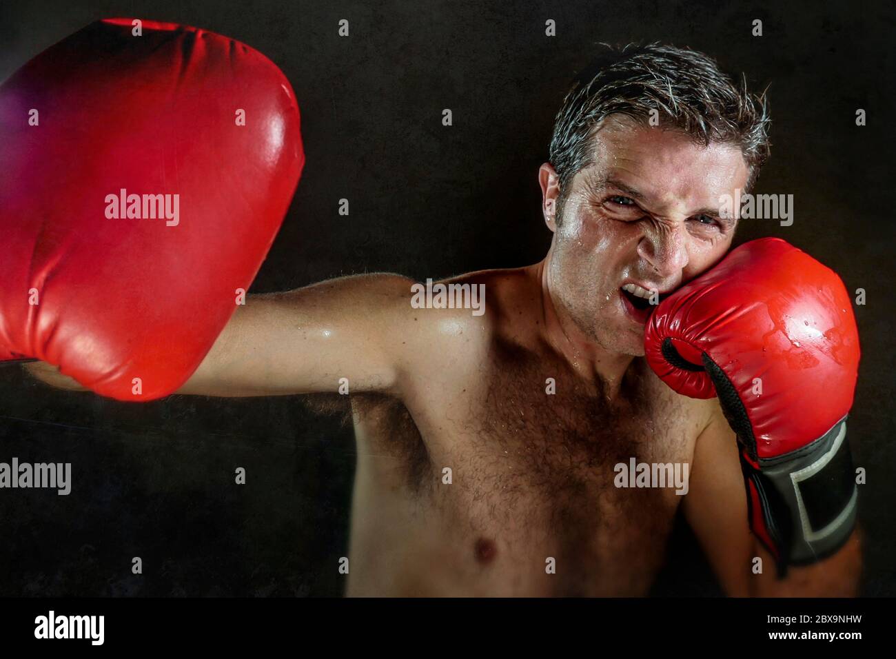 jeune homme de sport en colère et féroce en gants de boxe posant dans badass style de combattant cool et furieux throwin crochchet punch isolé sur le backgroun noir Banque D'Images