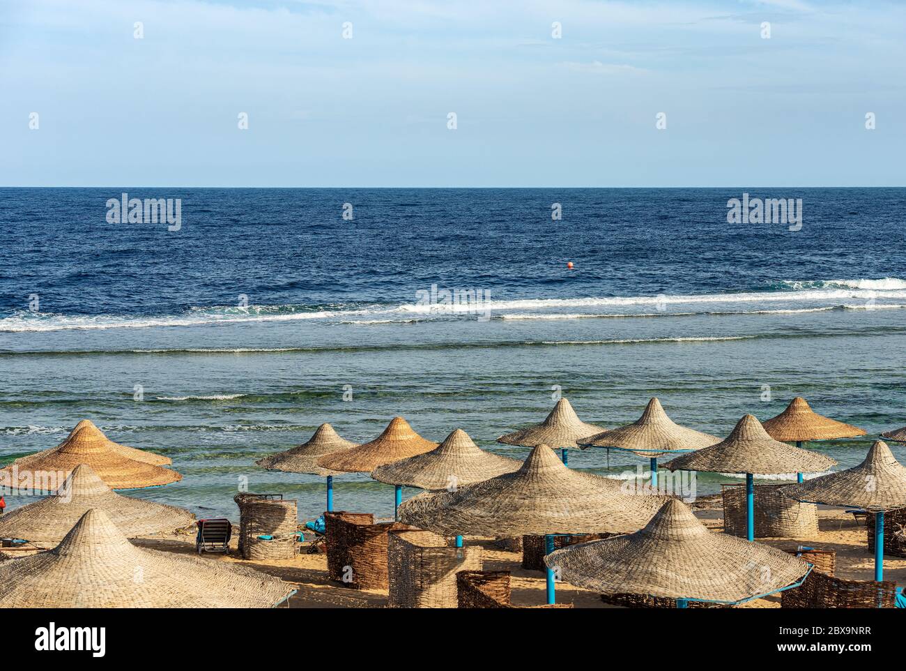 Plage de la mer Rouge avec parasols en paille près de Marsa Alam, Egypte, Afrique. Les vagues de la mer se sont écrachées sur le récif de corail Banque D'Images