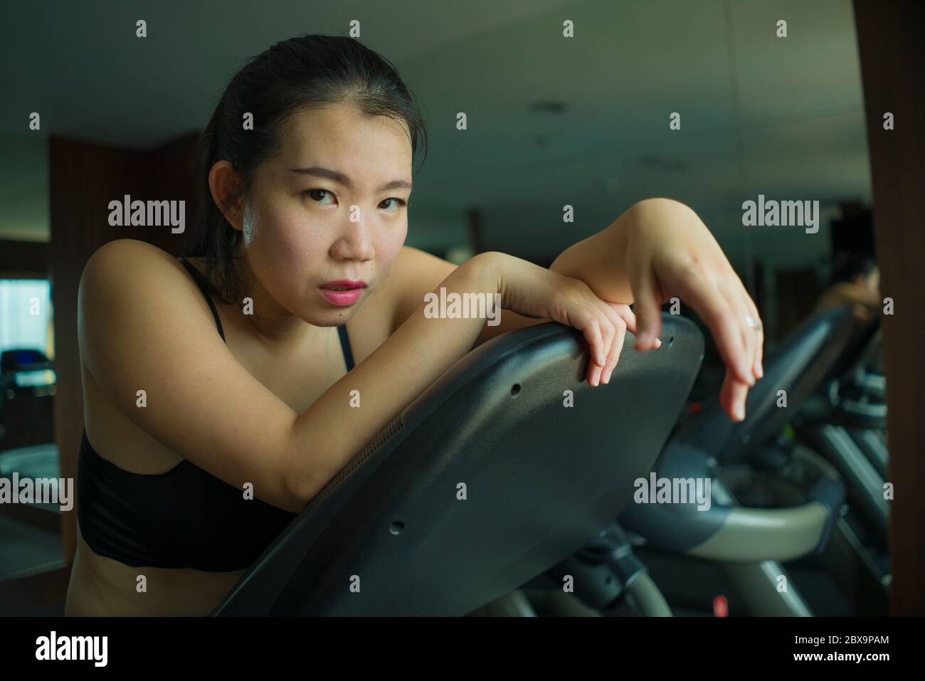 Jeune femme chinoise asiatique attirante et en forme épuisé pendant l'entraînement à la salle de gym de l'hôtel ou au club de fitness jogging dans l'entraînement de tapis roulant dur avec tir Banque D'Images
