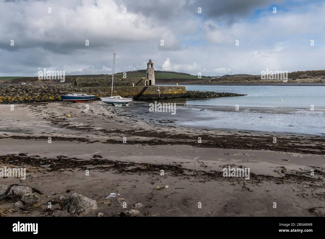 Plage de sable avec yachts au sol et jetée avec clocher Thomas Telford à Port Logan, Dumfries & Galloway, Écosse, Royaume-Uni. Banque D'Images
