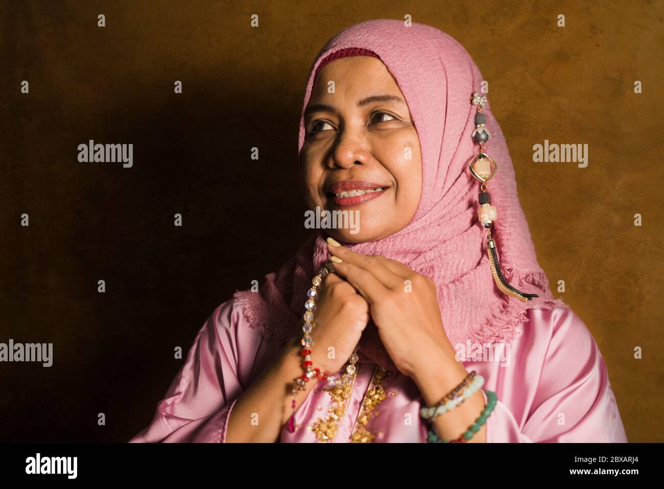 Portrait isolé en studio d'une femme musulmane âgée heureuse et positive dans ses années 50 portant un foulard hijab traditionnel de l'Islam priant en tenant des perles de prière Banque D'Images