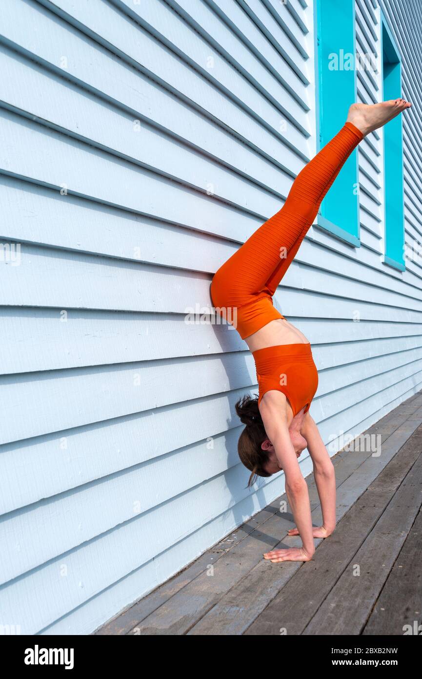 femme portant des vêtements de sport orange faisant une béquille de porte contre un mur bleu. Banque D'Images
