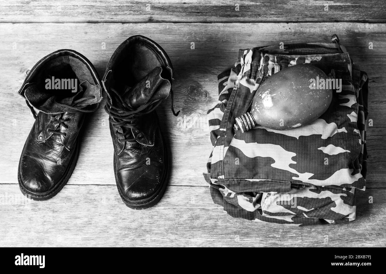 bottes militaires noires en cuir ancien, uniforme militaire et ballon d'eau sur fond de bois, vue rapprochée d'en haut, photo en noir et blanc Banque D'Images