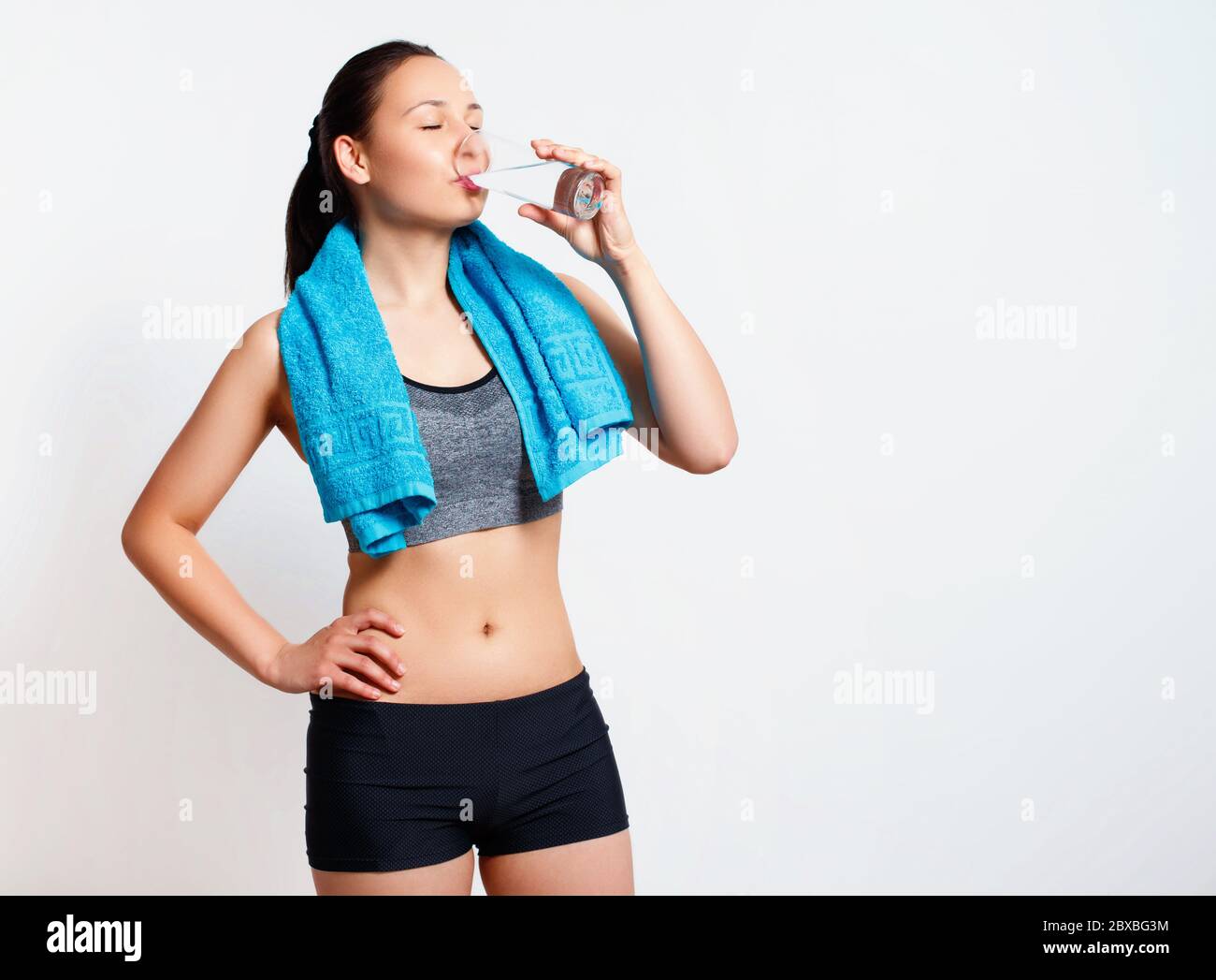 après l'entraînement, la femme boit de l'eau sur un verre. sur fond blanc. Banque D'Images