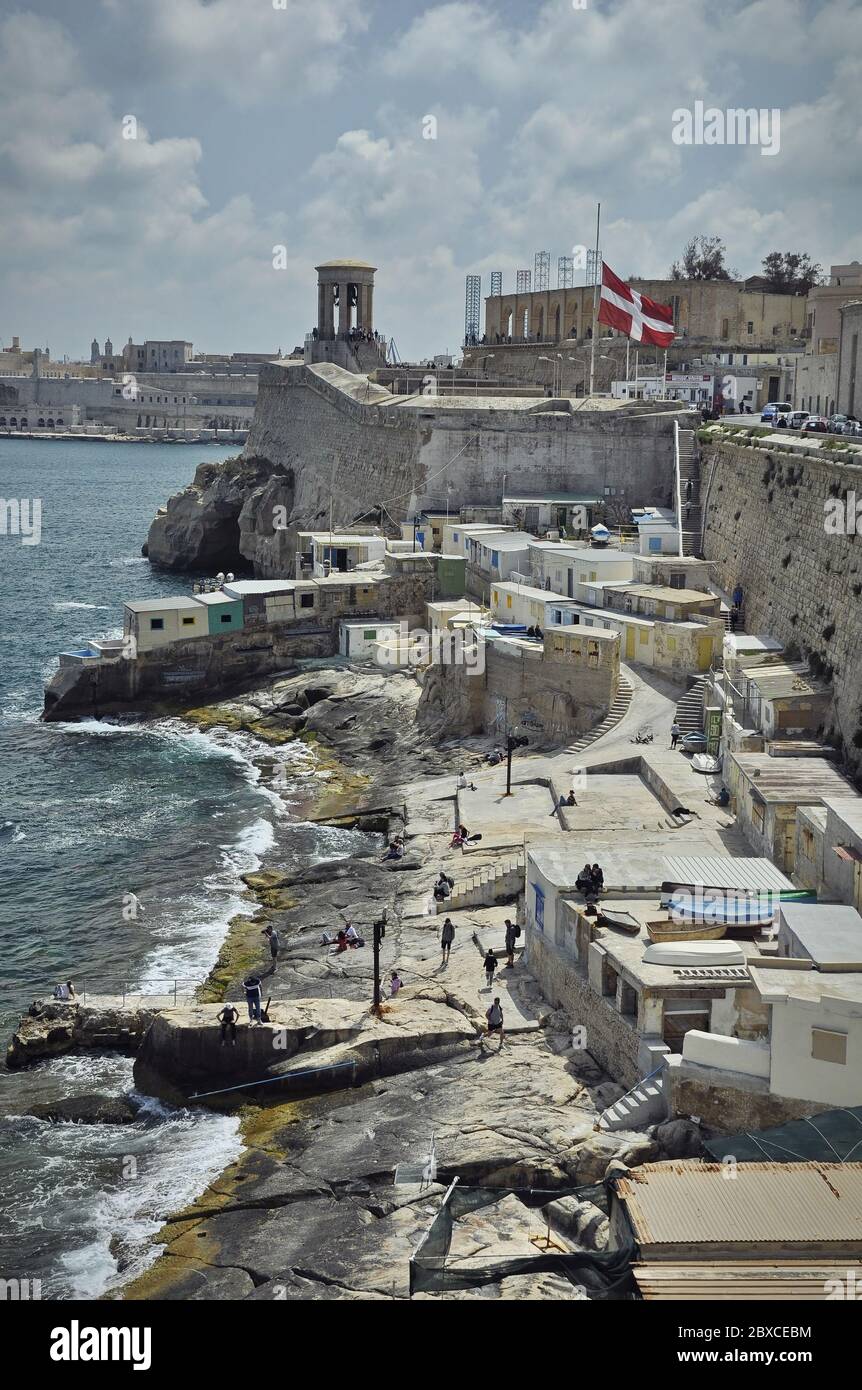 La côte avec des casernes blanches au milieu. Le front de mer est à gauche, le siège du Bell et un drapeau maltais sont à l'arrière Banque D'Images