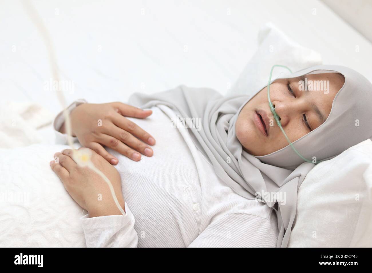 Patiente musulmane asiatique avec canule nasale séjournant dans la chambre d'hôpital seule. Une femme malade désagréable semble pensive au lit. Tube d'oxygène sur elle Banque D'Images