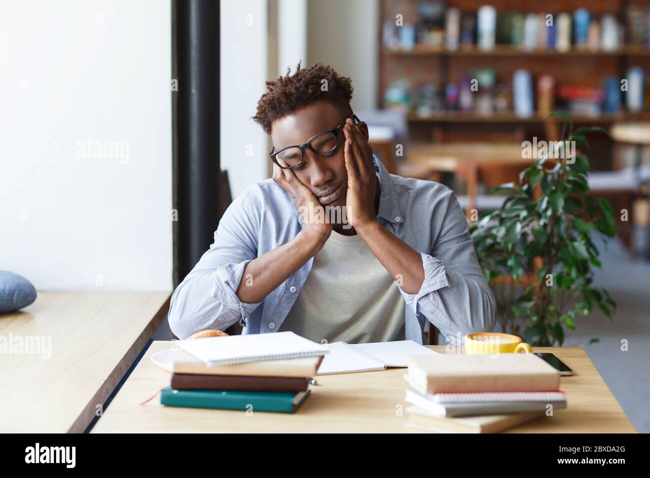 Un étudiant afro-américain épuisé se prépare à un examen difficile dans une cantine universitaire Banque D'Images