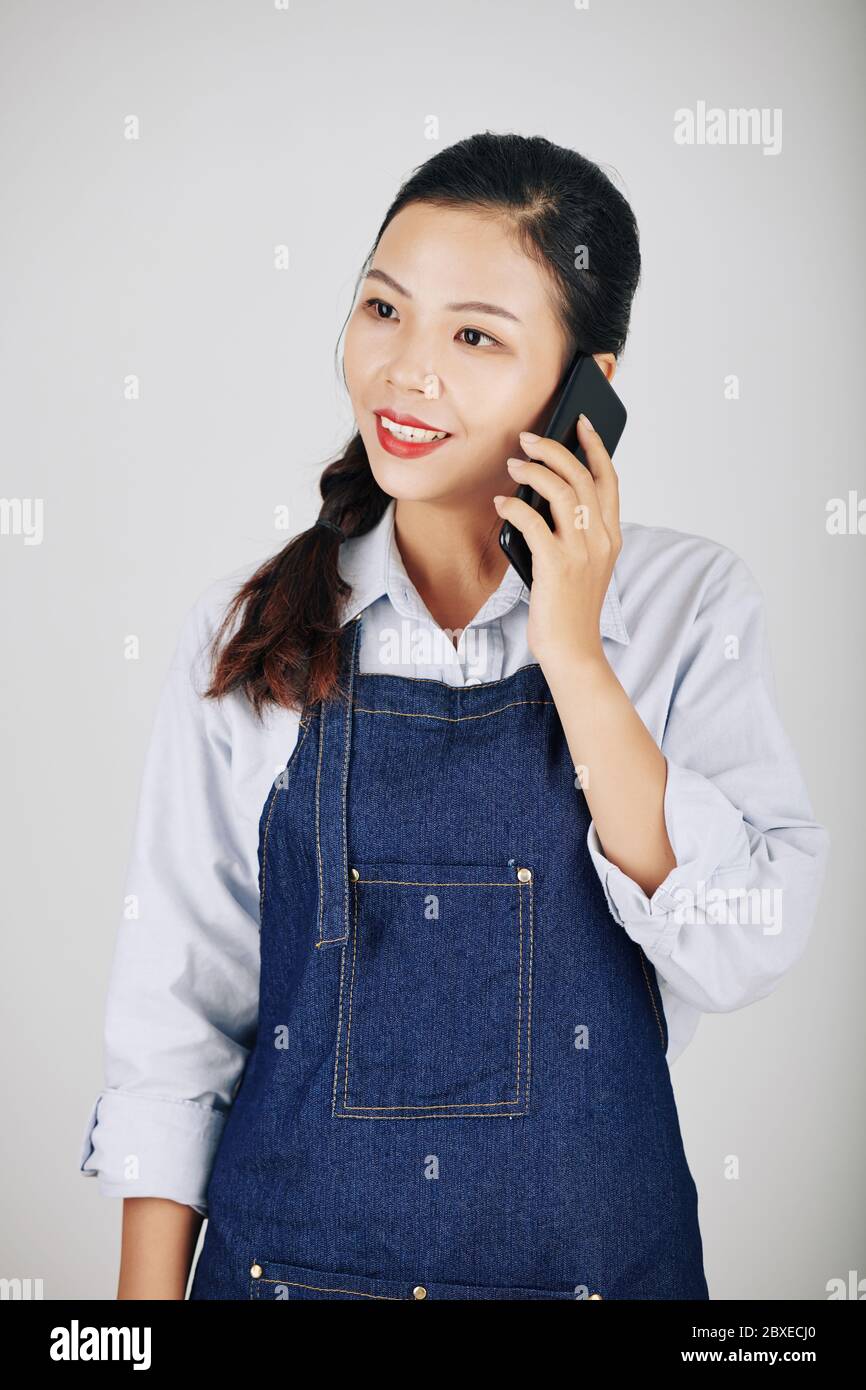 Portrait du propriétaire souriant du café ou de la serveuse en tablier en denim acceptant la commande par téléphone Banque D'Images