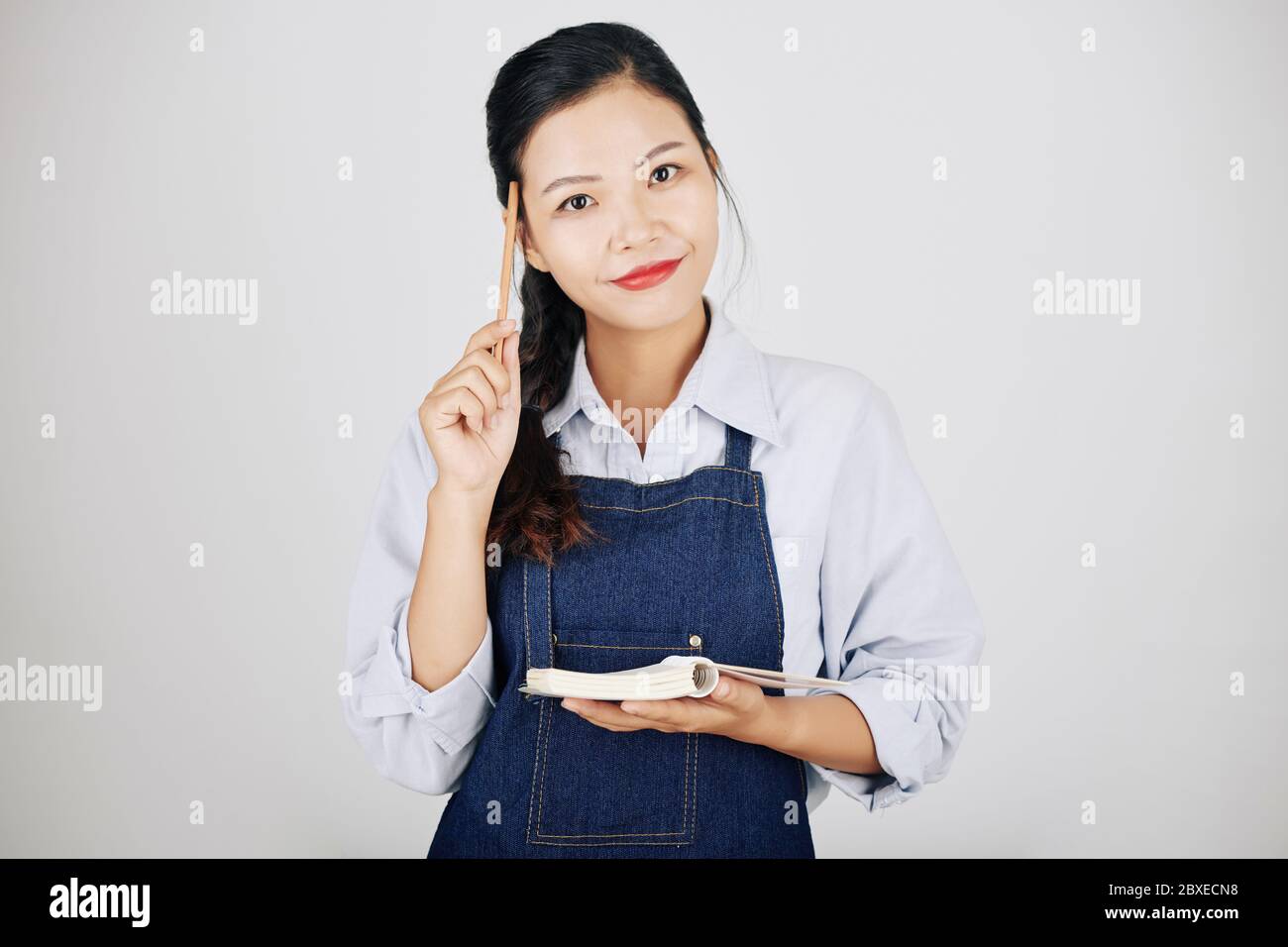 Bonne serveuse positive gratter le front avec un crayon et écrire l'ordre dans le manuel Banque D'Images