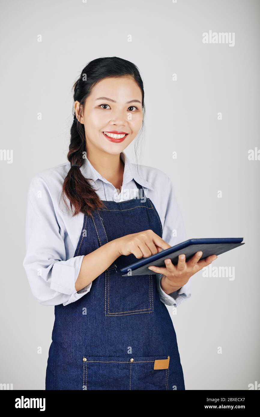 Portrait de la serveuse asiatique souriante utilisant l'application sur un ordinateur tablette lors de l'acceptation de la commande Banque D'Images