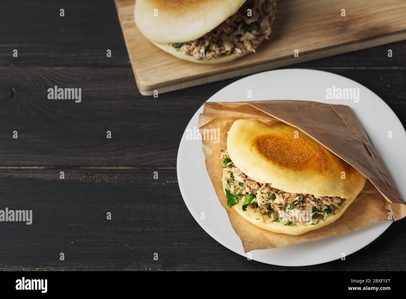 Rou jia Mo hamburger chinois est une cuisine populaire de rue. Sur la photo, un sandwich fait maison est présenté dans une assiette blanche sur une table en bois noir. Vue de dessus. Copier l'espace. Banque D'Images
