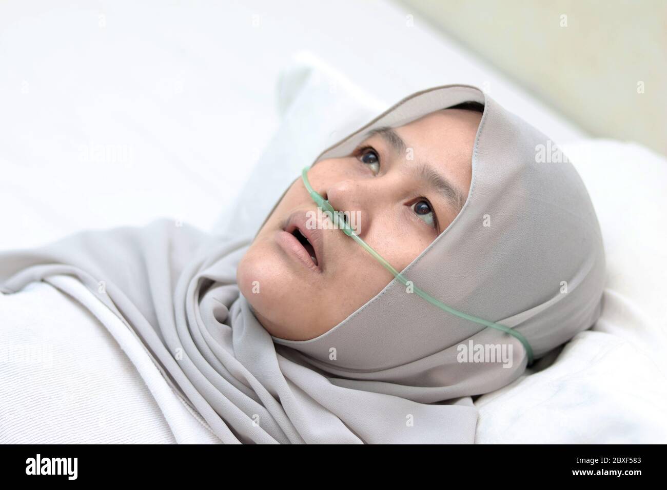 Patiente musulmane asiatique avec canule nasale séjournant dans la chambre d'hôpital seule. Une femme malade désagréable semble pensive au lit. Tube d'oxygène sur elle Banque D'Images