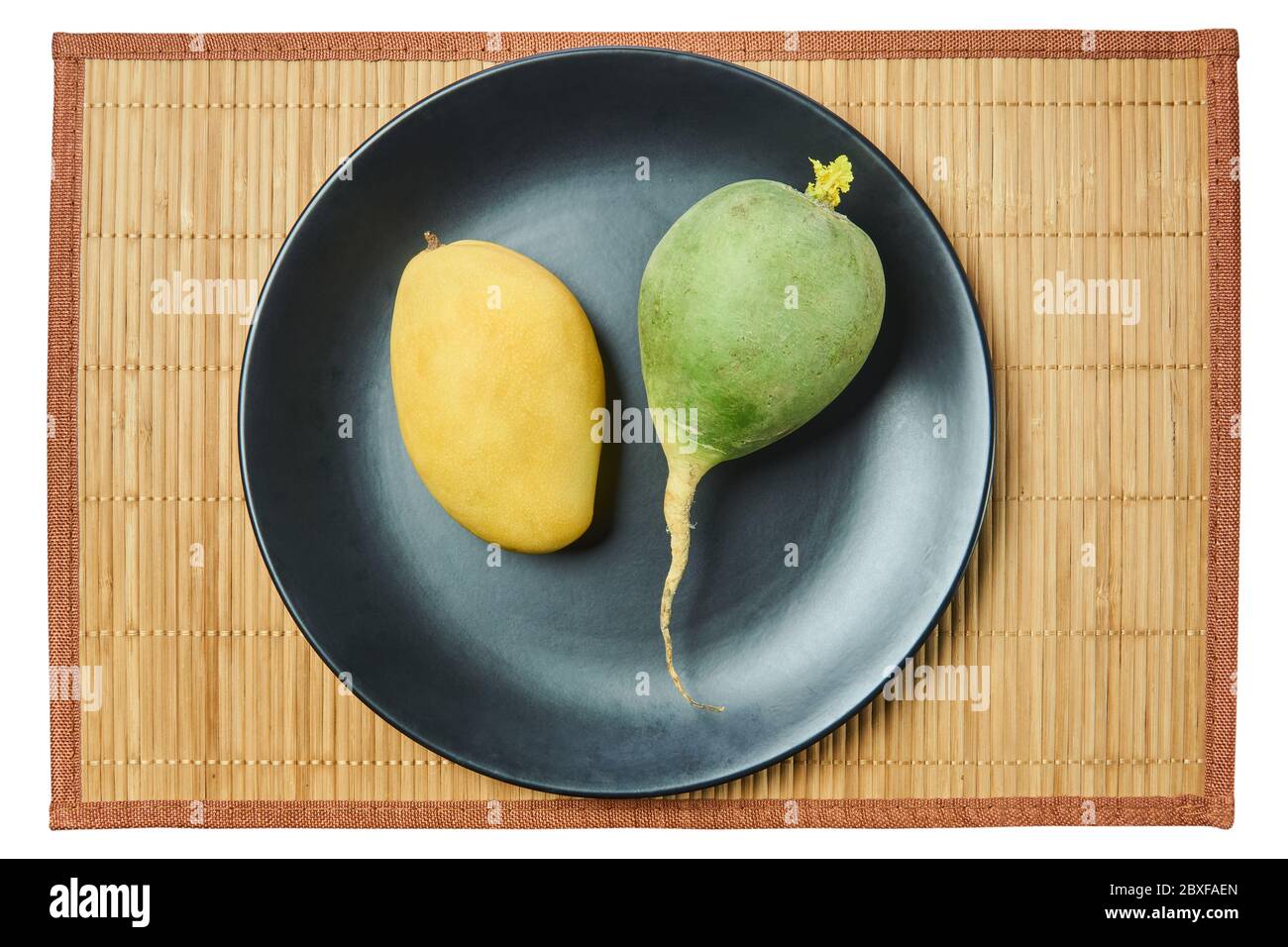 couleur encore vie - radis vert pâle et délicat fruit de mangue jaune sur une plaque grise sur un tapis de canne Banque D'Images