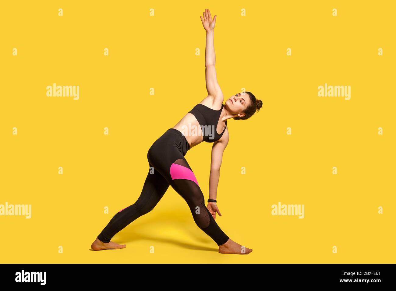 Posture du triangle. Femme athlétique mince avec cheveux bun dans serré vêtements de sport pratiquant le yoga, faisant l'exercice Trikonasana, se plier et étirer les muscles. Plein Banque D'Images