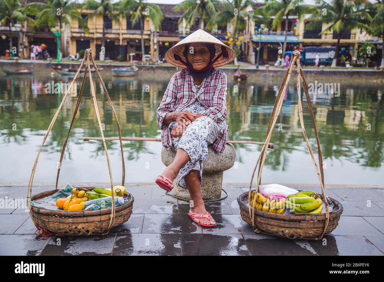 HOI AN, VIETNAM - 27 MARS 2017 : une dame âgée qui attend à côté de la rivière à Hoi une vente de fruits. Banque D'Images