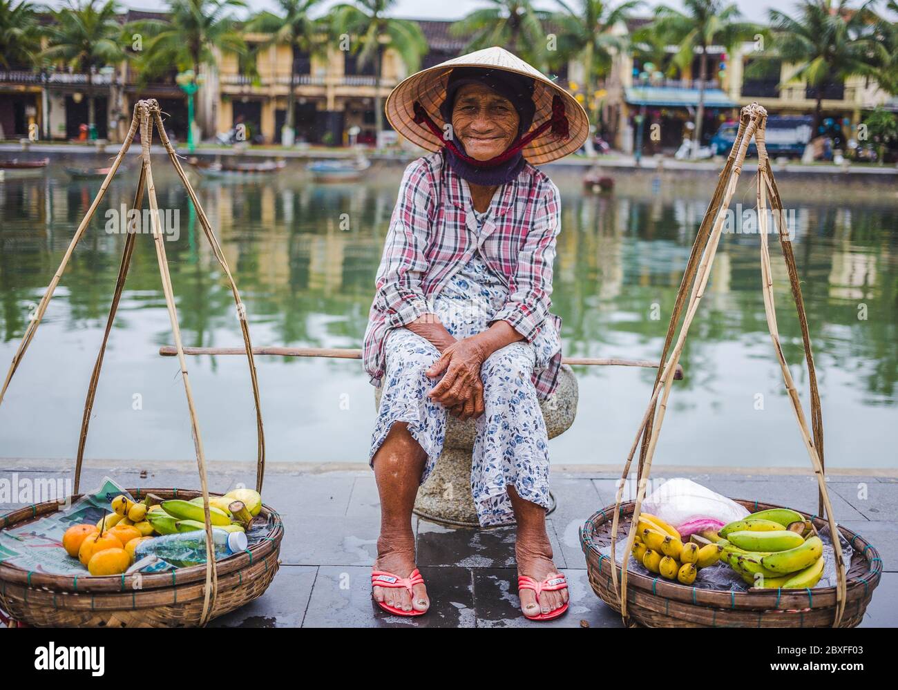 HOI AN, VIETNAM - 27 MARS 2017 : une dame âgée qui attend à côté de la rivière à Hoi une vente de fruits. Banque D'Images