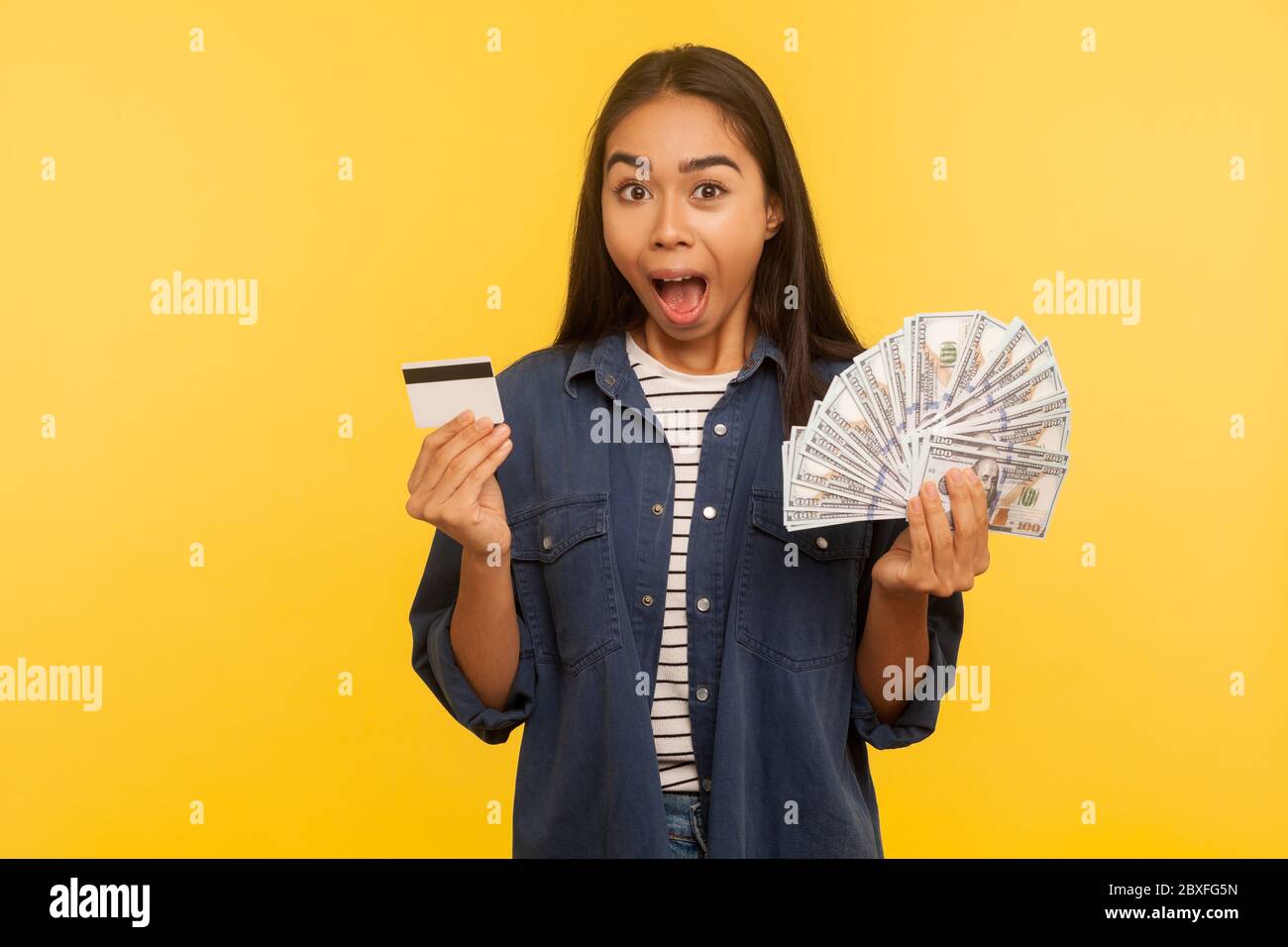 Wow, dépôt bancaire incroyable! Portrait d'une fille surprise en chemise denim tenant une carte de crédit et des billets de banque, criant dans l'étonnement, exp choqué Banque D'Images