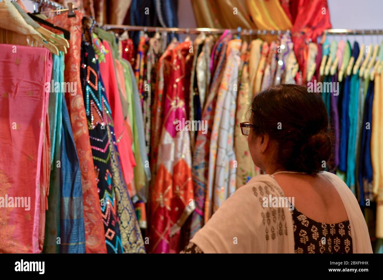 Une femme indienne âgée portant des lunettes vérifiant le designer kurta ( Salwar Kamiz) exposée dans un magasin de Dilli Haat ou Sarojini nagar marché à New Delhi Banque D'Images