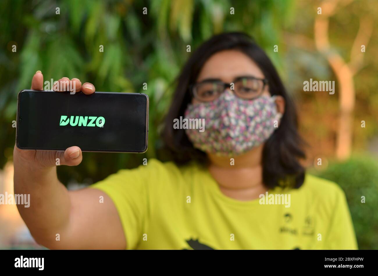 New Delhi, Inde, 2020. Fille portant un masque avec logo de l'application Dunzo Delivery brillant sur l'écran du téléphone mobile dans ses mains. Mise au point sélective et faible profondeur Banque D'Images