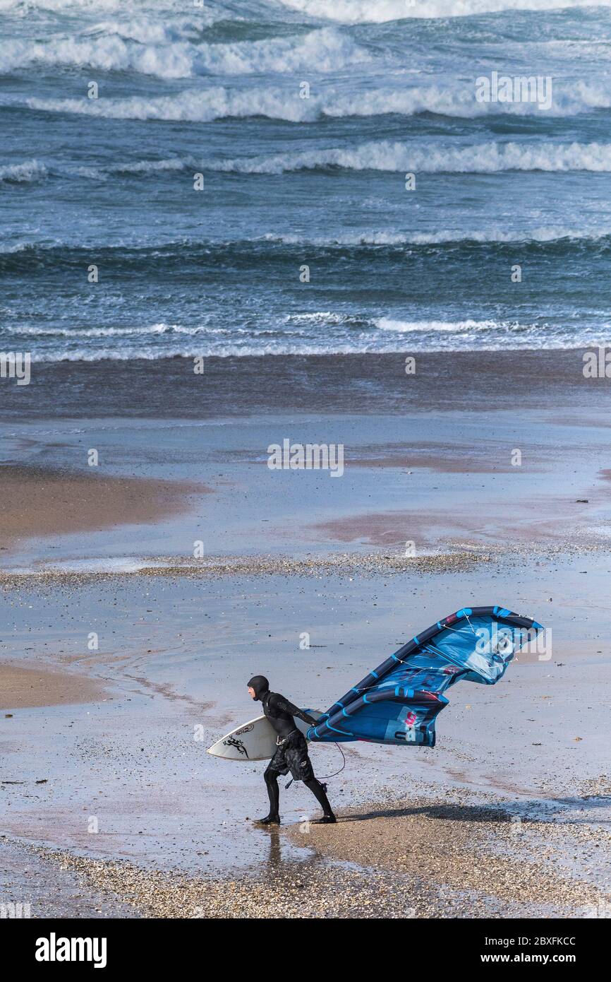 Un surfeur de kite-boarder transportant son équipement de kite-board surf dans les vents forts sur la plage de Fistral à Newquay, dans les Cornouailles. Banque D'Images