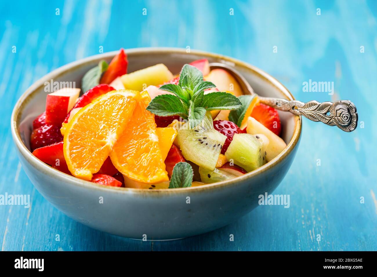 Salade de fruits frais pleine de vitamines pour l'été avec menthe sur fond bleu Banque D'Images