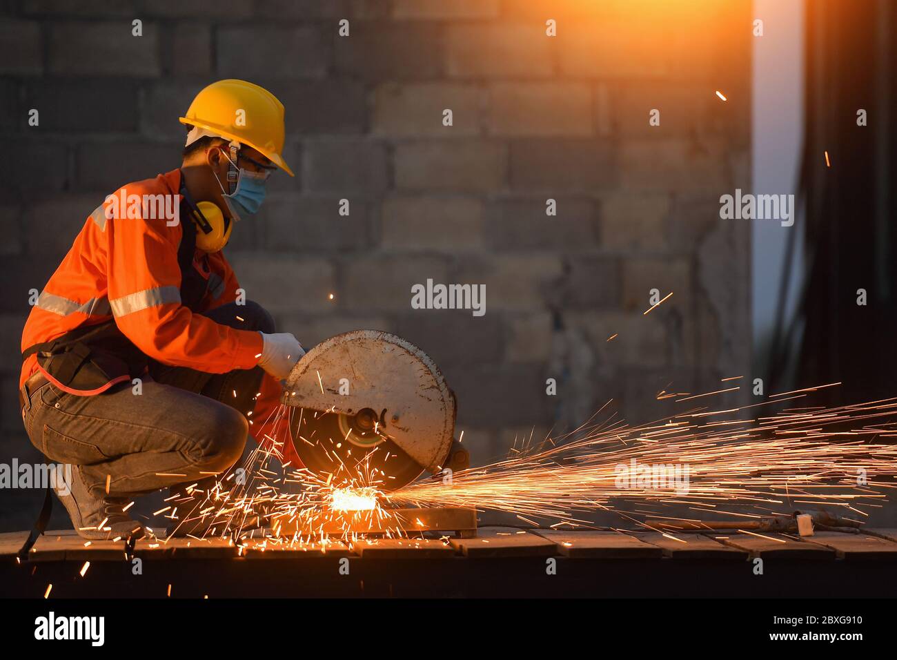 Travailleur industriel portant un masque facial coupant du métal avec une meuleuse métallique Banque D'Images