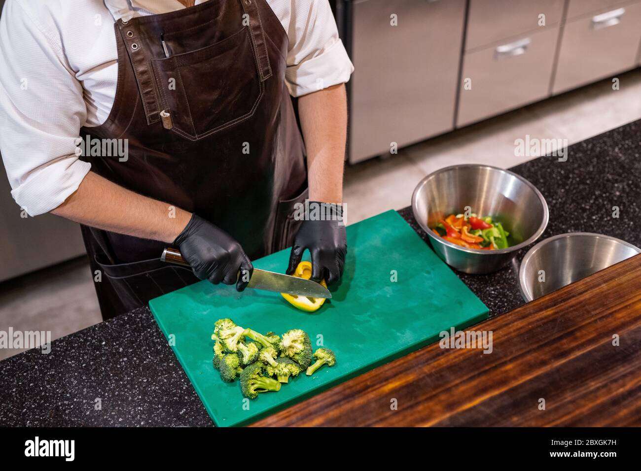 Vue ci-dessus d'un chef méconnaissable en tablier de cuir debout au comptoir et en coupant du poivron sur un plateau en plastique Banque D'Images