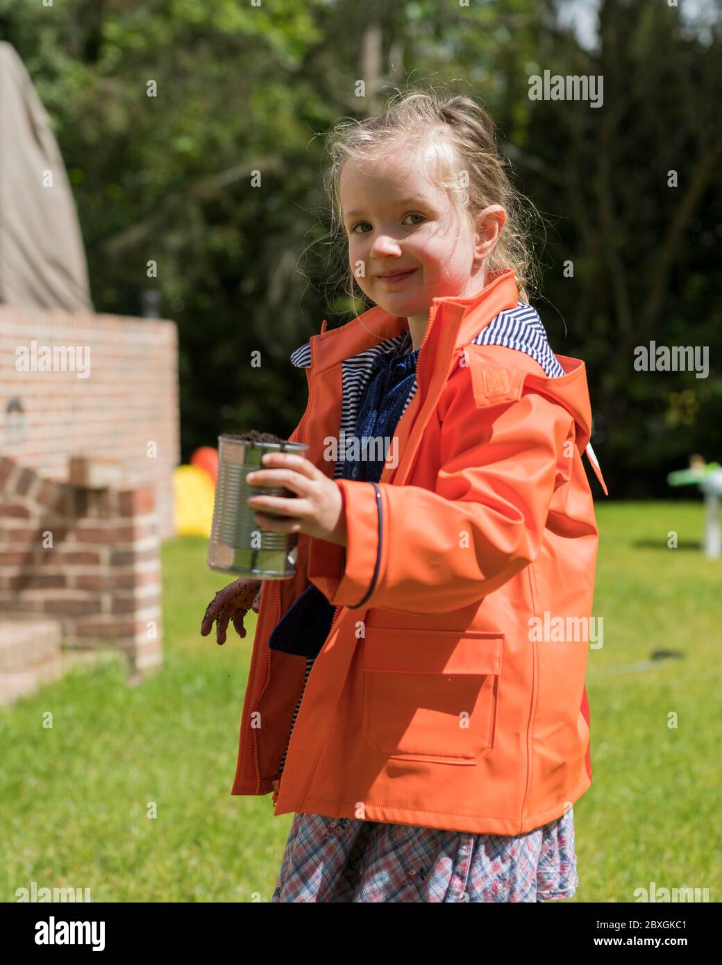 fille de 4 ans planter et jardiner, planter des plantes de concombre, porter un manteau de pluie orange/violet, jour ensoleillé, aide pré-école dans le jardin Banque D'Images