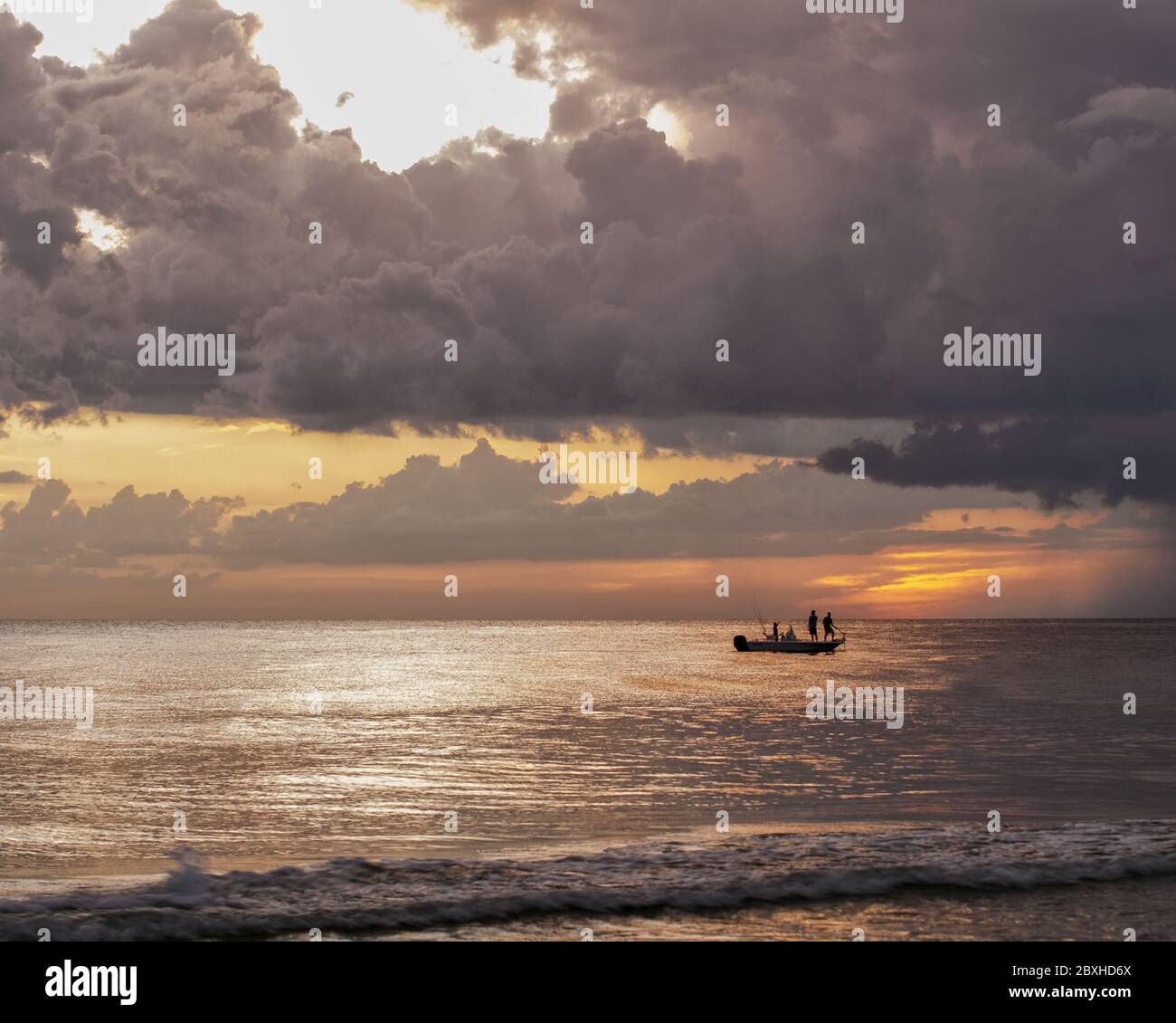 Coucher de soleil sur l'océan avec un bateau au loin avec deux personnes debout pour pêcher. Banque D'Images