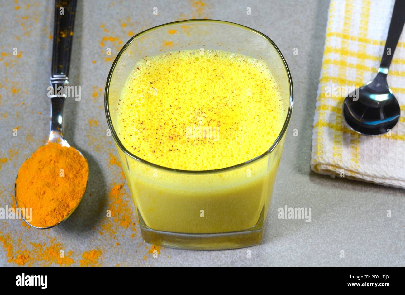 Lait curcuma également appelé lait doré dans une tasse de verre garni de poudre de cannelle Banque D'Images