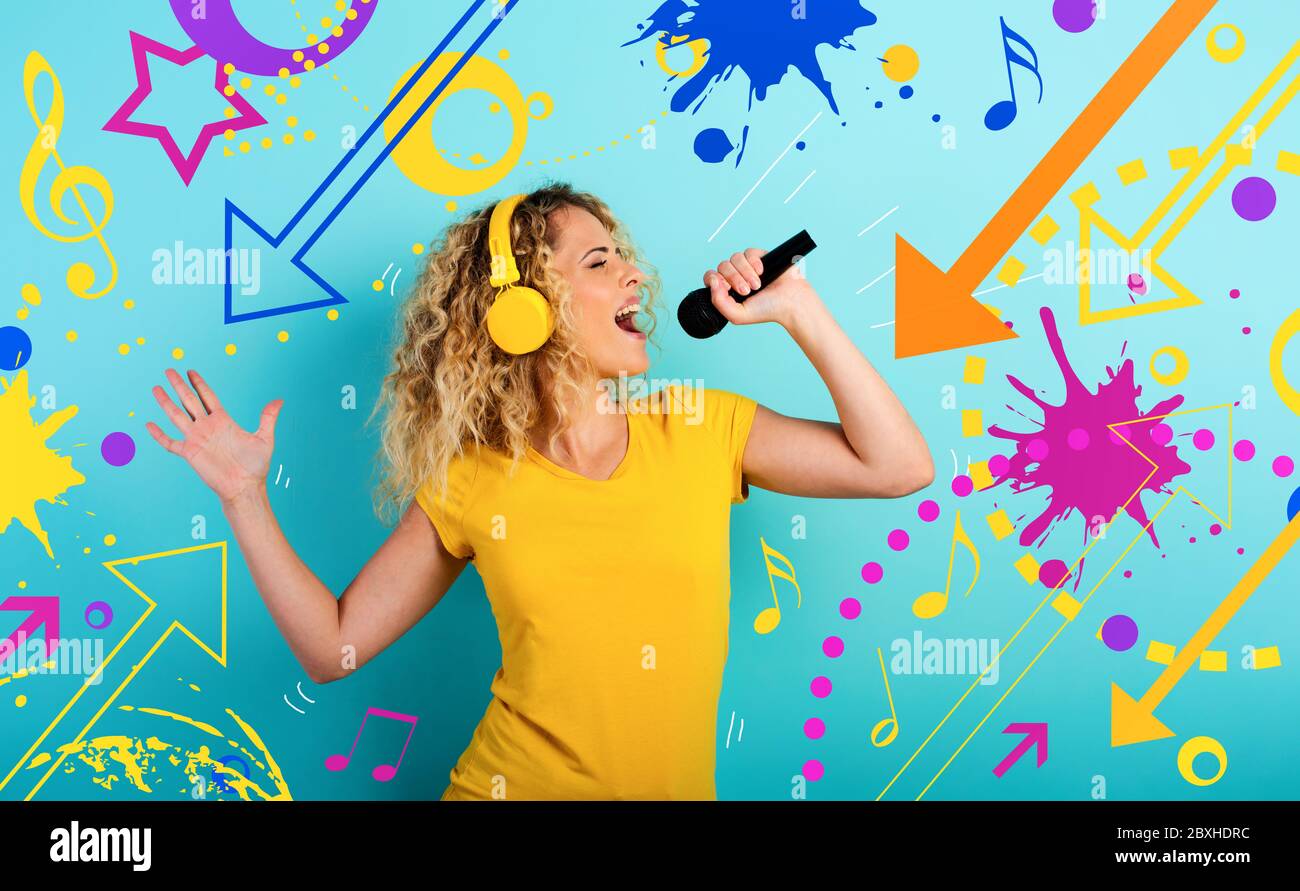 Une fille avec casque écoute de la musique et des chansons avec un microphone. Expression émotionnelle et énergique. Fond cyan Banque D'Images