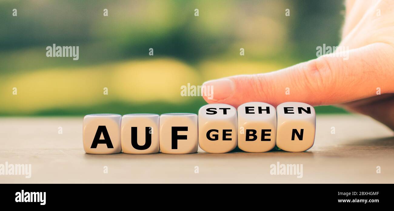 La main tourne les dés et change l'expression allemande 'aufgeben' ('abandonner') en 'aufstehen' ('se lever'). Banque D'Images