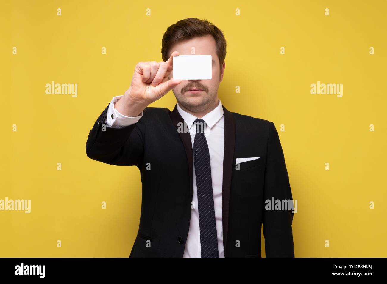 Homme caucasien en costume montrant la carte de visite donnant un geste parfait ou ok. Studio tourné sur un mur jaune. Banque D'Images